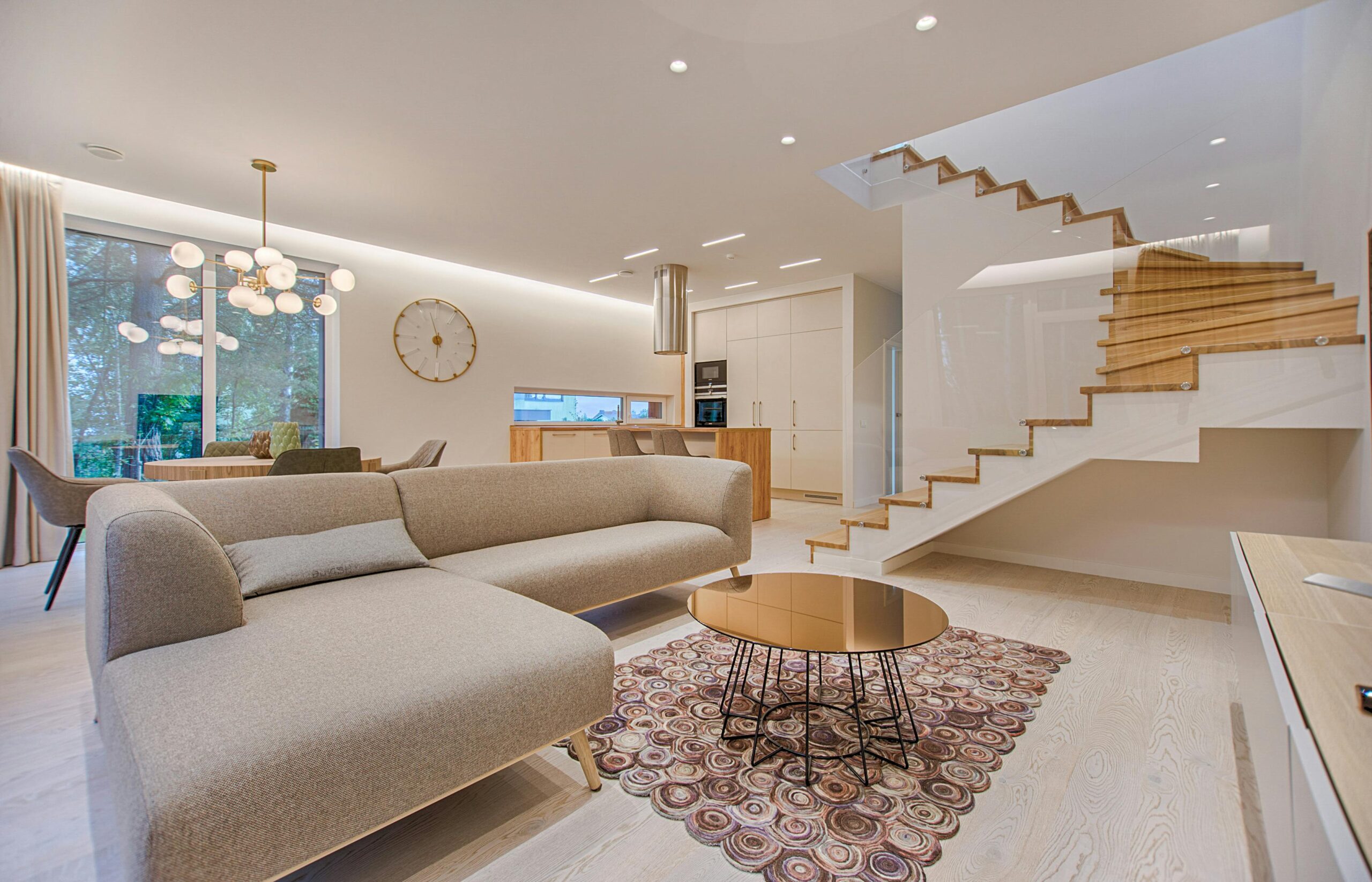 Modern living room with beige sectional sofa and wooden staircase.